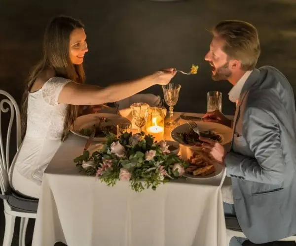 woman feeding man with fork on romantic candlelight dinner. Top perspective honeymoon, vacation romance